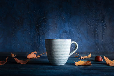 A cup of tea with autumn leaves in front of a window with rain behind it, with a place for text