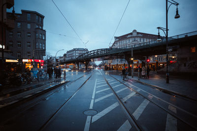 People on railroad tracks in city against sky