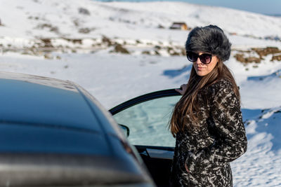 Young woman wearing sunglasses while sitting on car