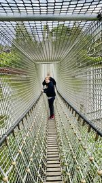 Teenage boy crossing a river by a small  footbridge made out of rope and wood