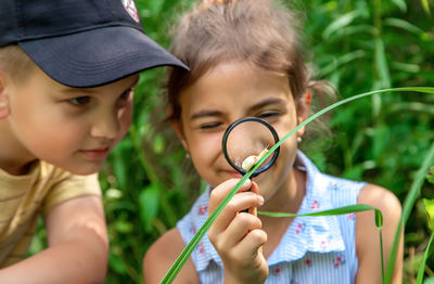 Smiling girl looking snail on grass through magnifying glass by brother