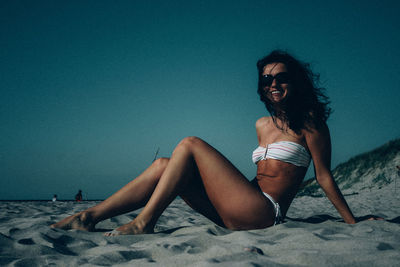 Side view of woman wearing sunglasses sitting at beach