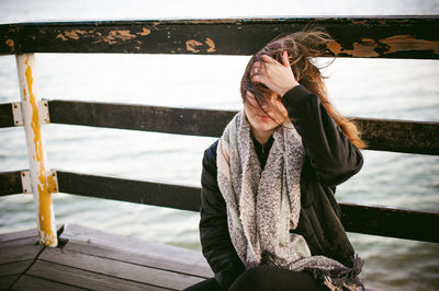 Thoughtful young woman with hand in hair sitting on pier over sea