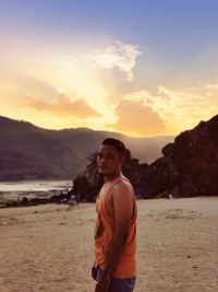 Young man standing on beach against sky during sunset