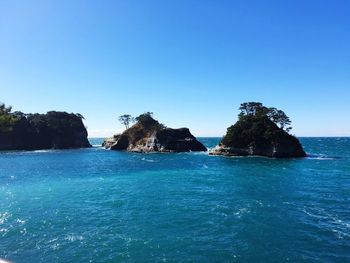 Scenic view of rocks and sea against clear blue sky