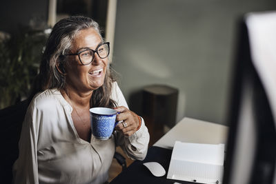 Mature businesswoman holding cup while doing video call at home office