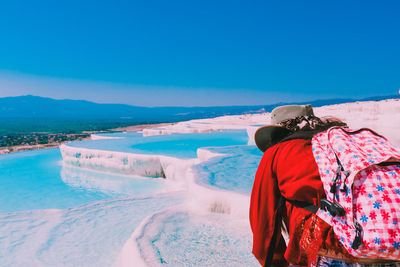 Rear view of person on snow covered landscape against blue sky