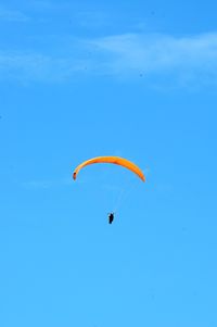 Low angle view of person paragliding against blue sky