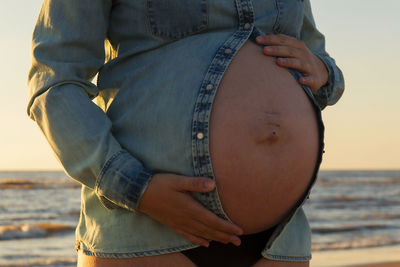 Close-up of pregnant woman touching belly while standing at beach