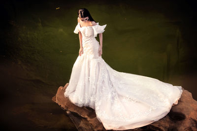 Bride standing by lake on rock