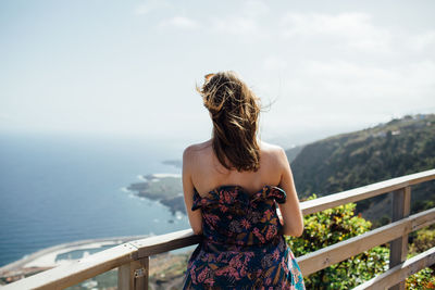 Rear view of woman standing by railing against sea