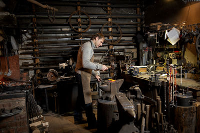 The blacksmith manually forging the red-hot metal on the anvil in smithy with spark fireworks