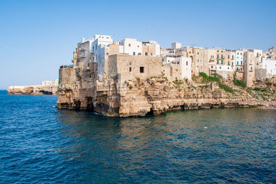 Buildings by sea against clear blue sky