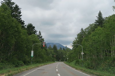 Empty road along trees and plants against sky