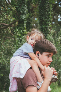 Brother carrying sister on shoulders in forest