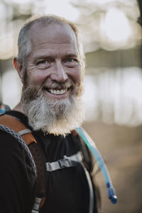 A smiling and happy retired man with a beard and a hiking backpack