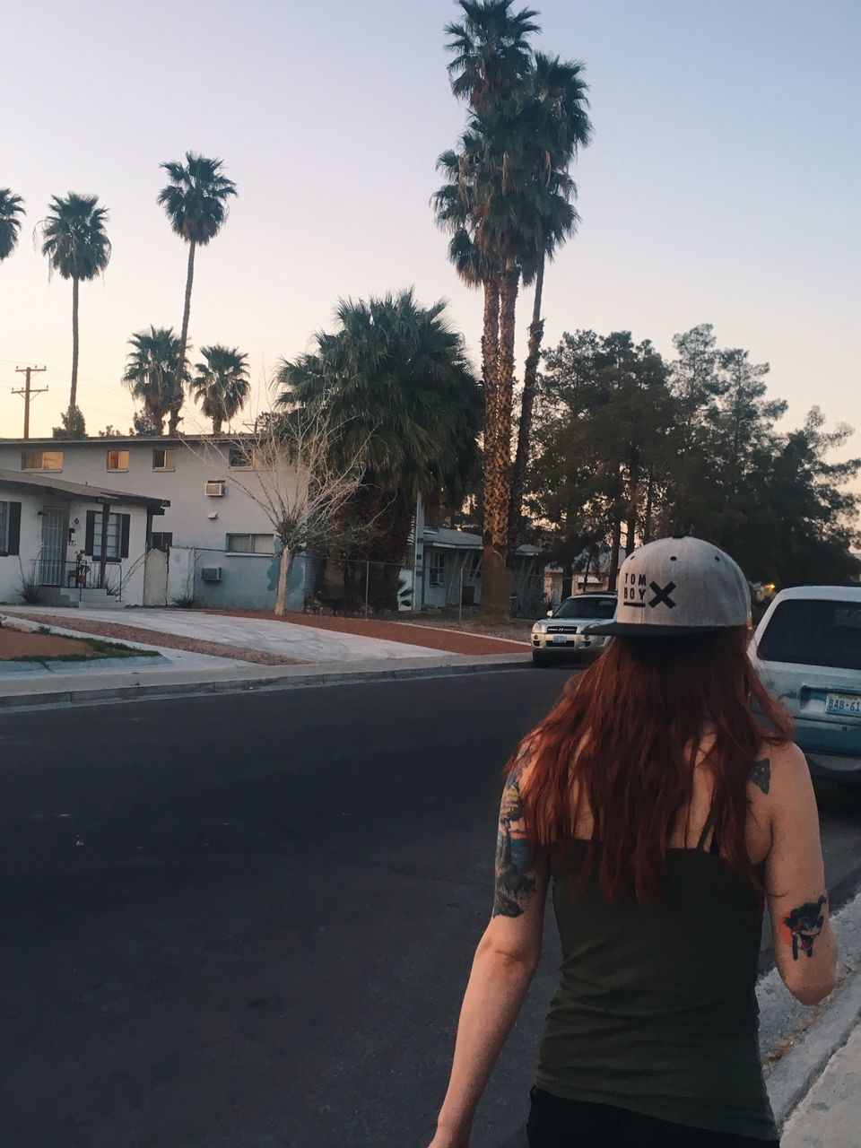 tree, one person, real people, palm tree, road, plant, city, tropical climate, lifestyles, leisure activity, transportation, street, rear view, sky, standing, three quarter length, nature, hairstyle, architecture, outdoors