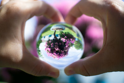 Cropped hands holding crystal ball against blooming flowers