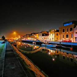 Illuminated buildings by canal against sky at night