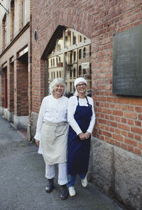 Portrait of smiling female bakers standing by brick wall outside bakery