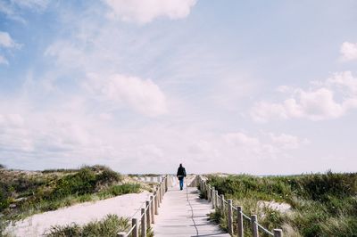 Rear view of people walking on landscape against sky
