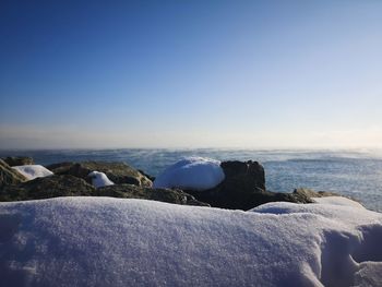 Rocks by sea against clear blue sky