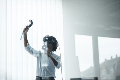 Young male professional wearing virtual reality headset playing with joystick in board room at office