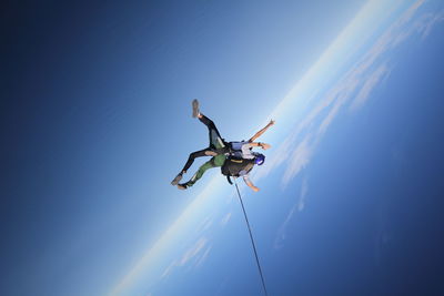 Low angle view of men paragliding against blue sky