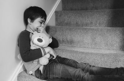 Boy holding teddy bear while sitting on steps