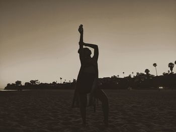 Silhouette woman with arms raised on beach against sky during sunset