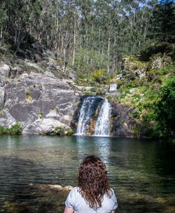 Rear view of person looking at waterfall in forest