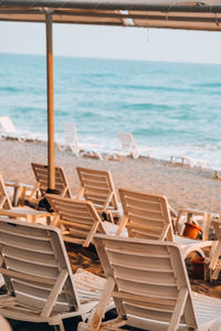 Chairs and tables on beach by sea against sky