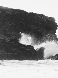 Sea waves splashing on mountain against clear sky