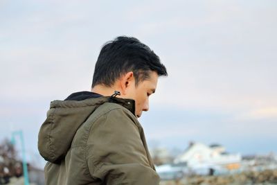 Side view of young man standing against sky