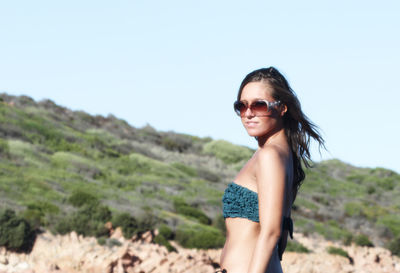 Portrait of smiling young woman standing on beach against clear sky