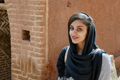 Portrait of smiling young woman standing against wall