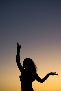 Silhouette woman with arms raised against sky during sunset