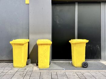 Yellow garbage bin on sidewalk against wall