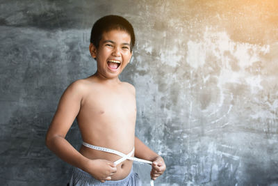 Portrait of cheerful boy holding measuring tape while standing against wall