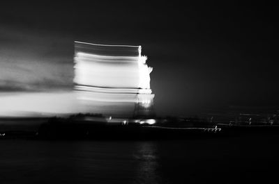 Reflection of illuminated built structure in water against sky at night
