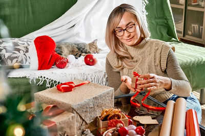 Blond woman wrapping presents in recycled card and decorated it with dried oranges and fir branches.