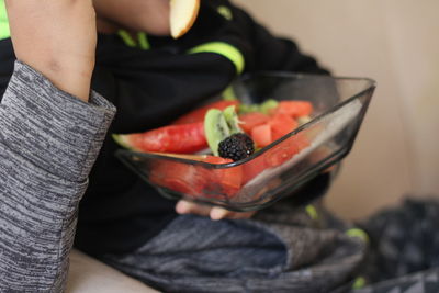 Midsection of boy eating fruits while sitting on sofa at home