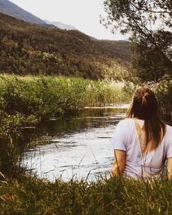 Rear view of woman sitting by lake against mountain