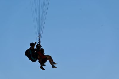 Low angle view of men paragliding against clear blue sky