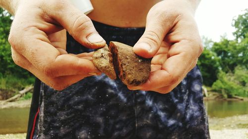 Midsection of boy holding stones at riverbank