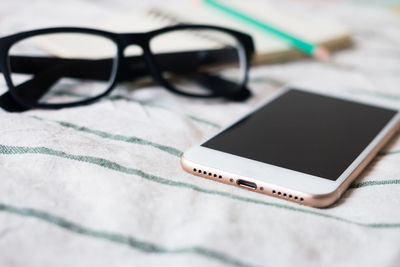 High angle view of smart phone with eyeglasses and diary on table