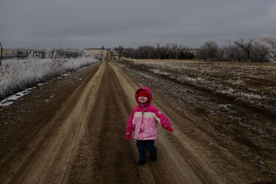 Girl wearing warm clothing on dirt road against sky