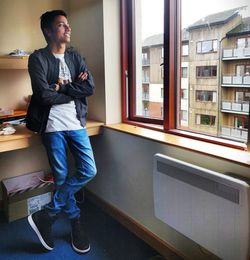 Young man looking away while standing against window
