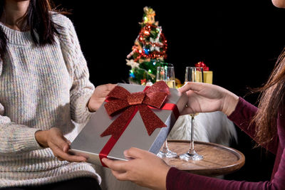 Midsection of women exchanging christmas gift against black background