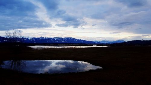 Scenic view of lake against cloudy sky during sunset